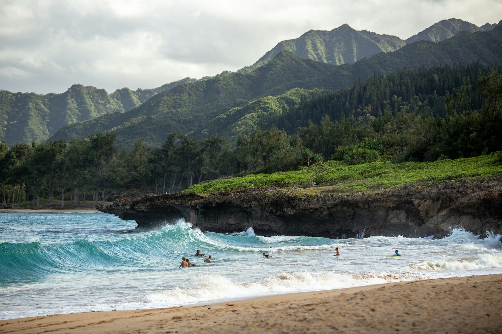 Waves rolling onto a beach beneath green Hawaiian mountains
