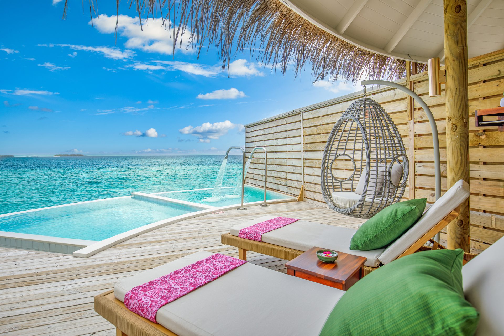 An overwater villa terrace with sun beds and a private plunge pool above the lagoon
