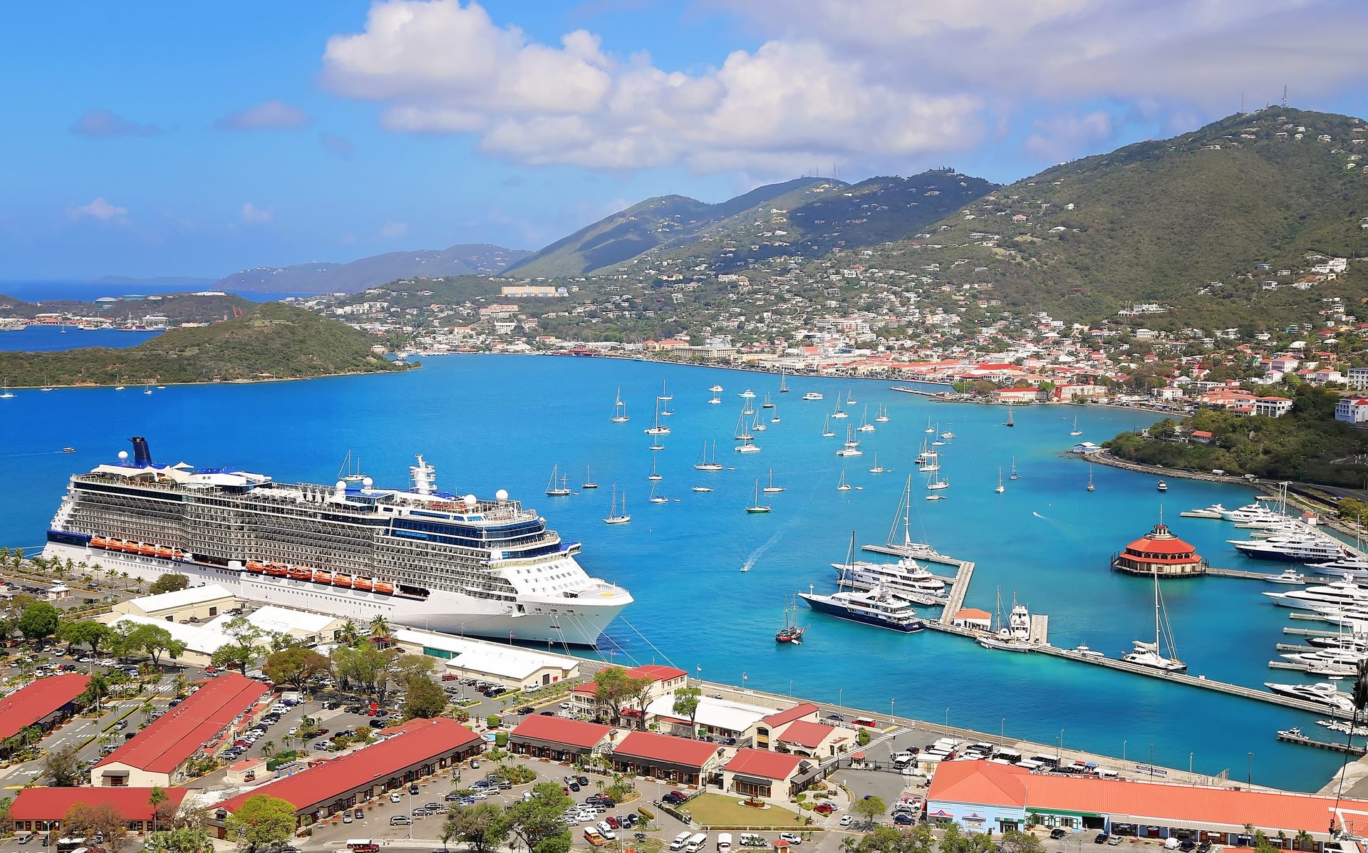 A cruise ship docked in a Caribbean harbor below green hills