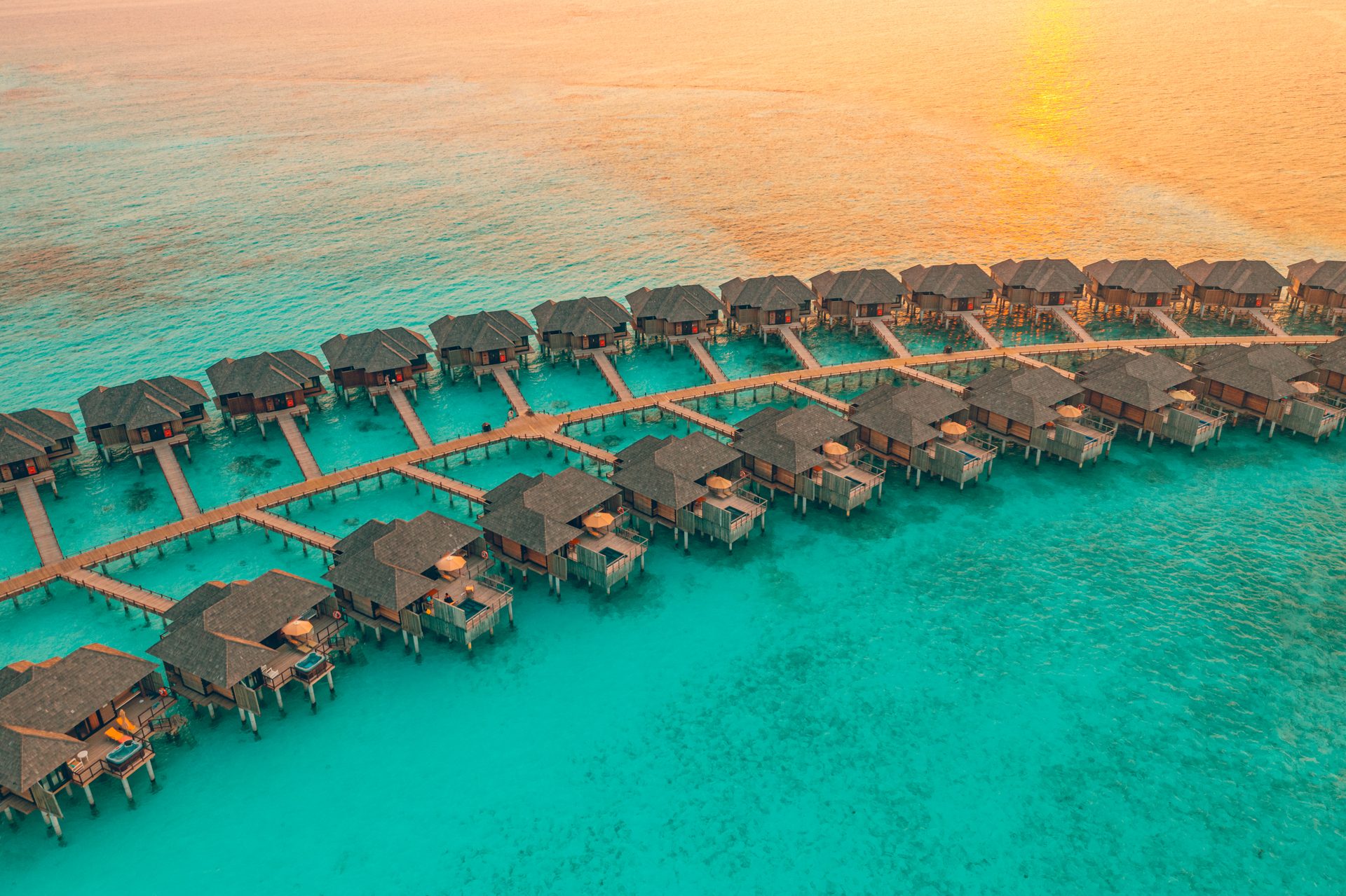An aerial view of overwater villas on a lagoon at sunset